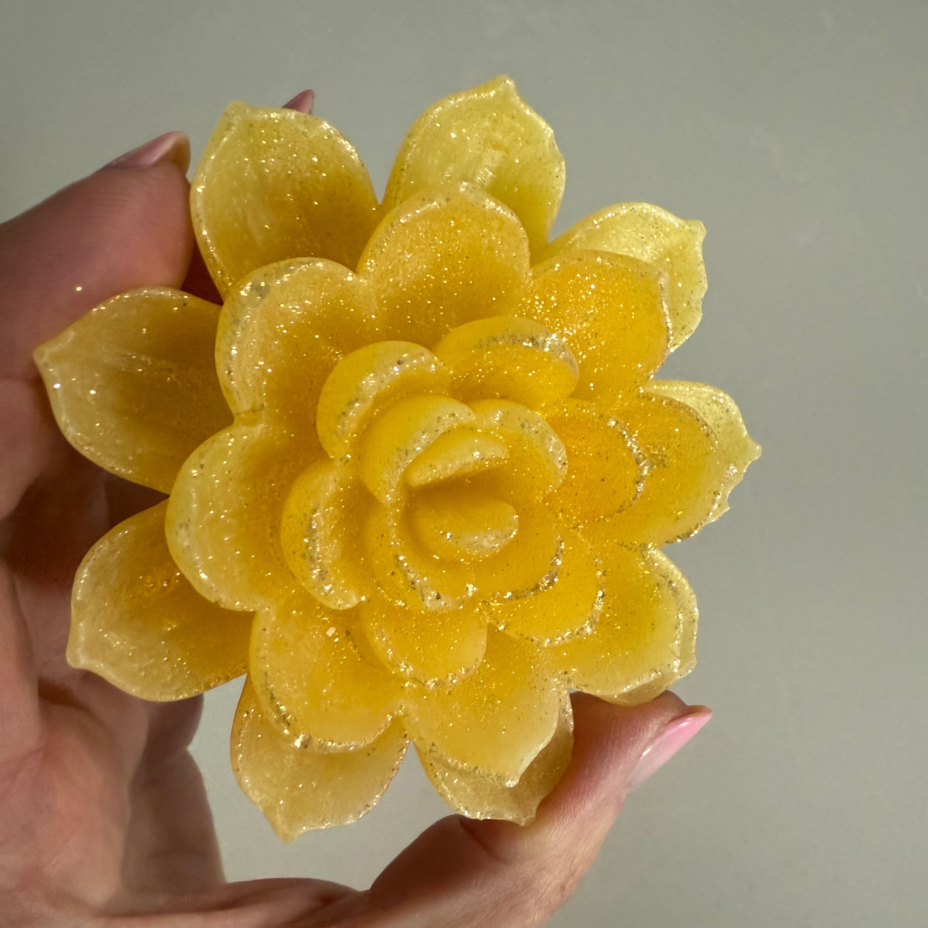 Yellow flower-shaped crystal candy held by a hand against a neutral background